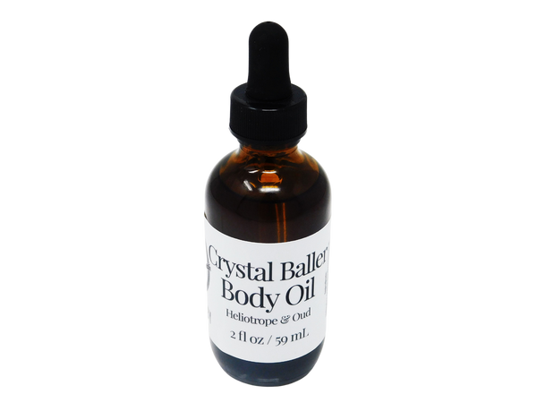 2 oz brown glass dropper bottle with white label that reads: Crystal Baller Body Oil. Heliotrope & Oud. 
