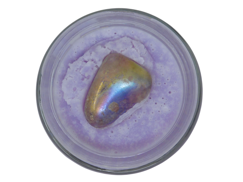 Iridescent stone in a container with purple body butter on a white background