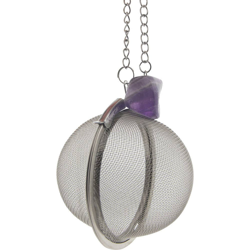 A stainless steel tea infuser ball with a purple amethyst crystal attached to the handle, suspended by a chain.