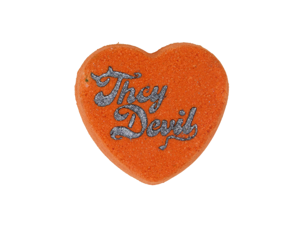 red heart bath bomb with 'they devil' airbrushed on top in dark glitter styled in a devilish font