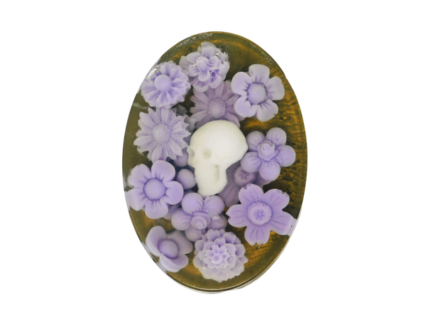 A gold oval shaped glycerin soap with a clear top that has a white skull and purple flower embeds and smells like a unique blend of snapdragon apples, golden pear, and wild thyme.