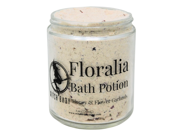 White powdery bath potion mixed with salts and flowers packaged in 8 oz glass jar with clear label that reads: Floralia Bath Potion. Honey & Flower Garlands.