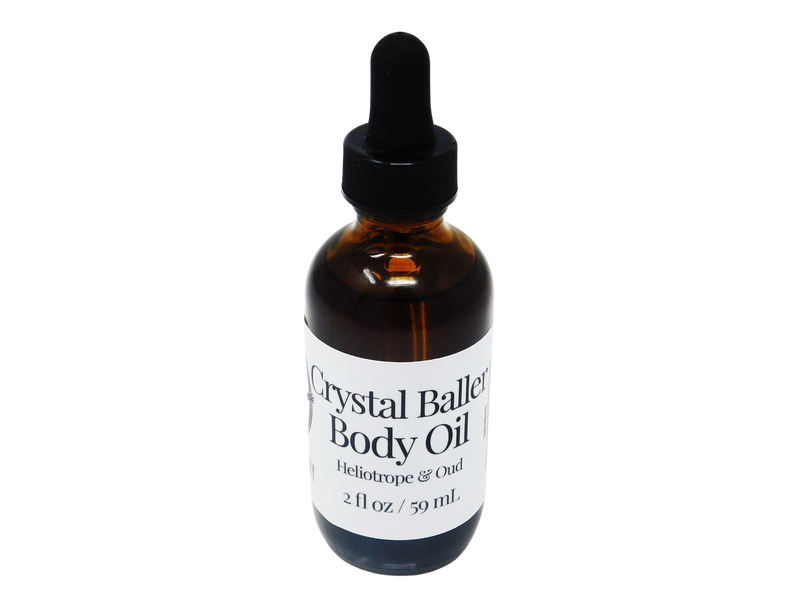 2 oz brown glass dropper bottle with white label that reads: Crystal Baller Body Oil. Heliotrope & Oud. 