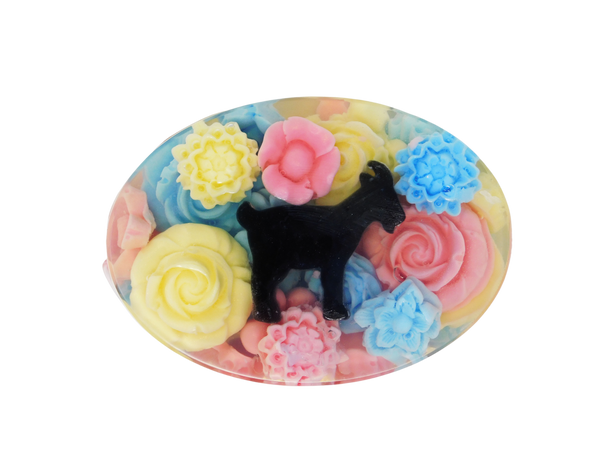 An oval shaped soap with pink, blue, and yellow flowers surrounding a goat embedded in a clear soap 