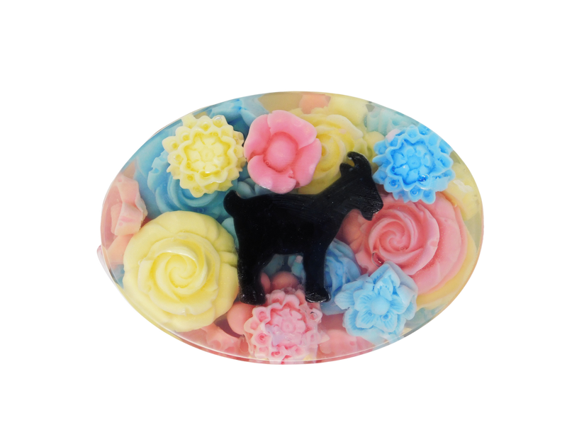 An oval shaped soap with pink, blue, and yellow flowers surrounding a goat embedded in a clear soap 